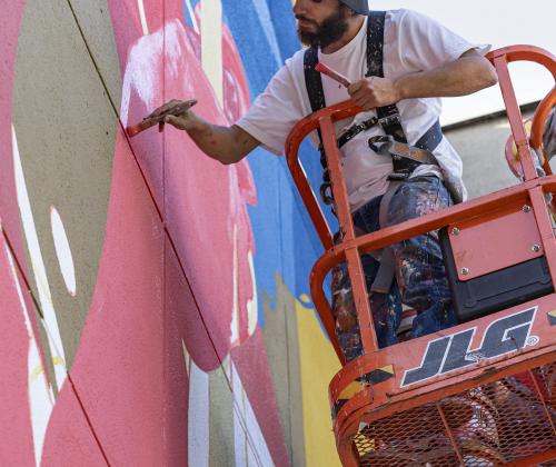 Zësar Bahamonte pintando el mural desde una plataforma elevadora