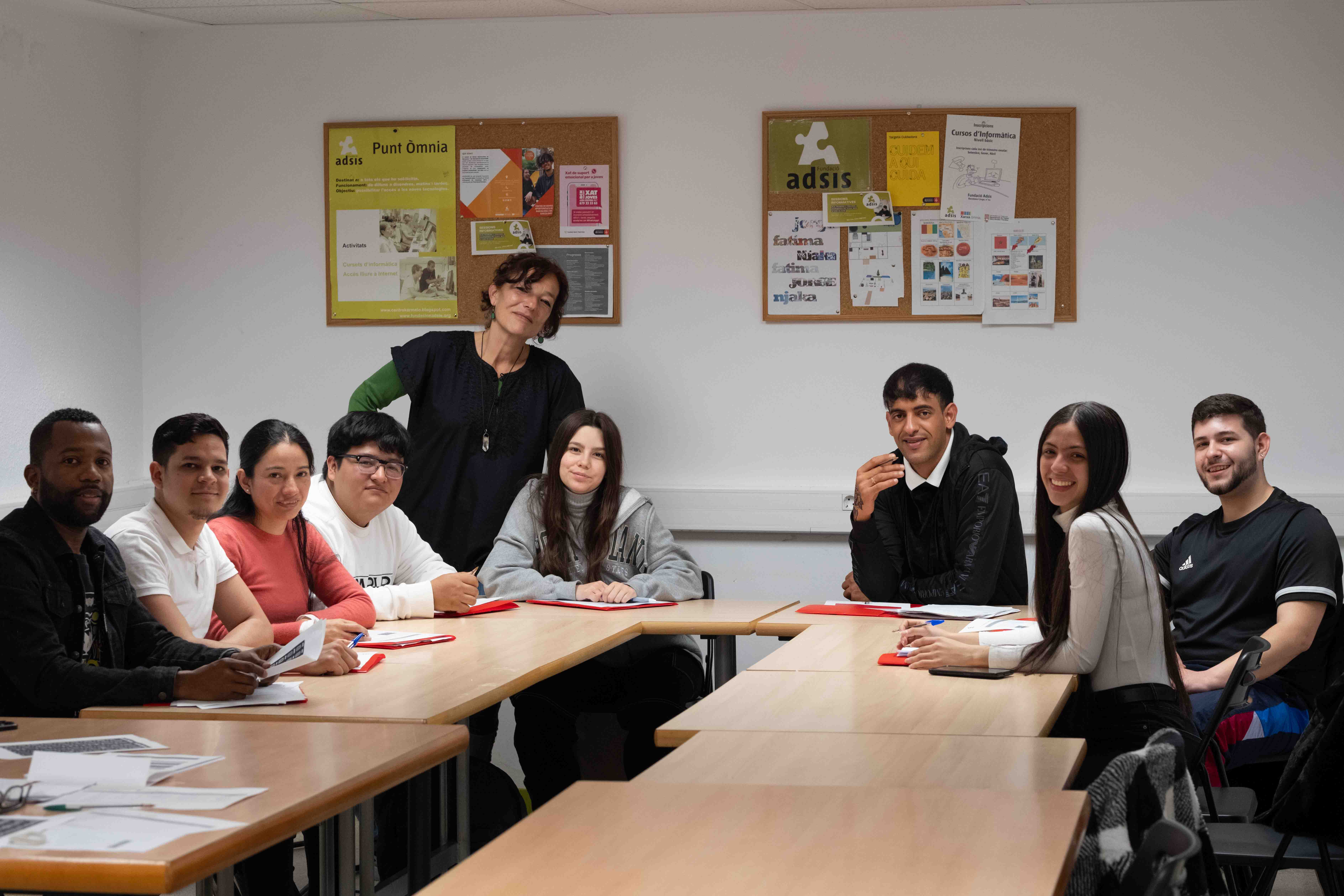 Un grupo de personas sentados en un aula mirando a cámara. Detrás, de pie, una persona formadora