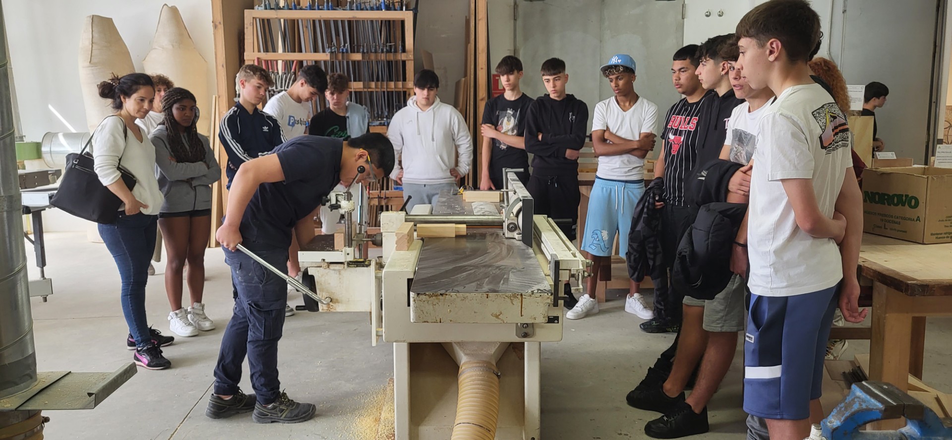 Un grupo de personas viendo a un chico trabajar en un taller de carpintería