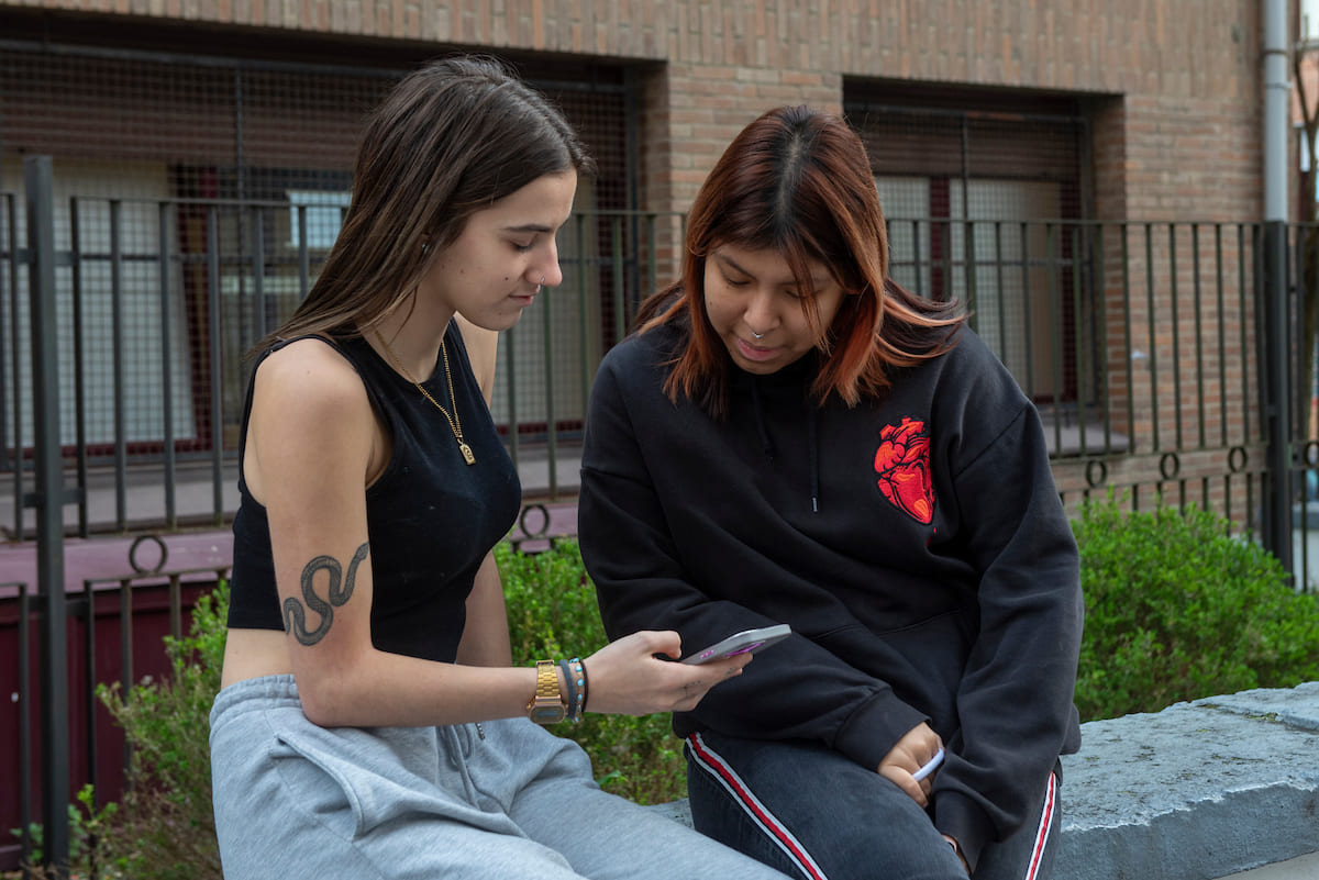 Dos jóvenes observan con curiosidad la pantalla de un móvil en un entorno urbano