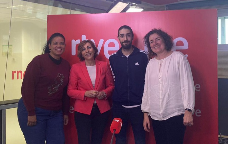 Cuatro personas posan de pie en un estudio de radio. Al fondo, en un cartel rojo se lee RTVE