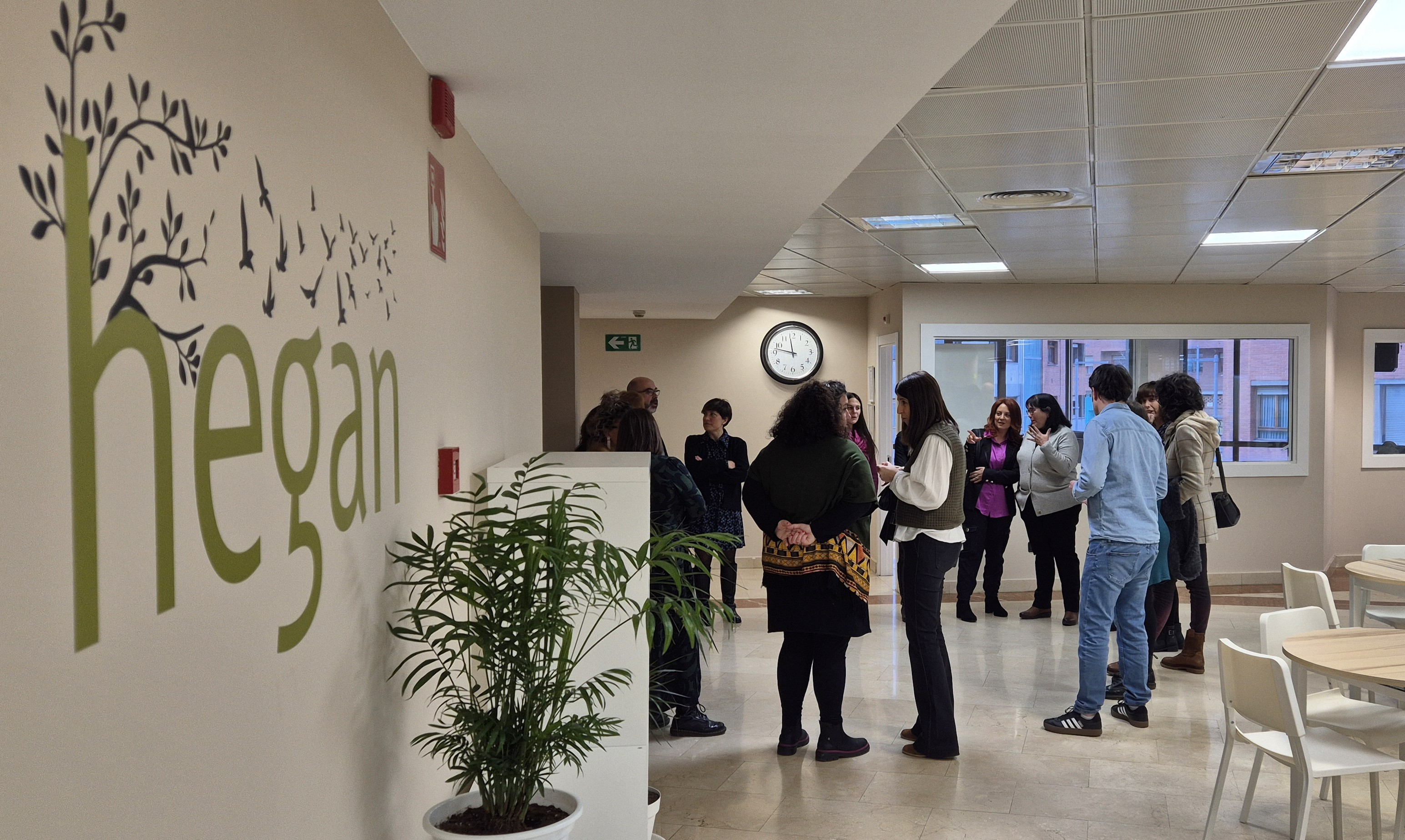 La sala principal del centro de día Hegan con el logo en la pared izquierda y un grupo de personas hablando al fodo, delante de unos despachos acristalados