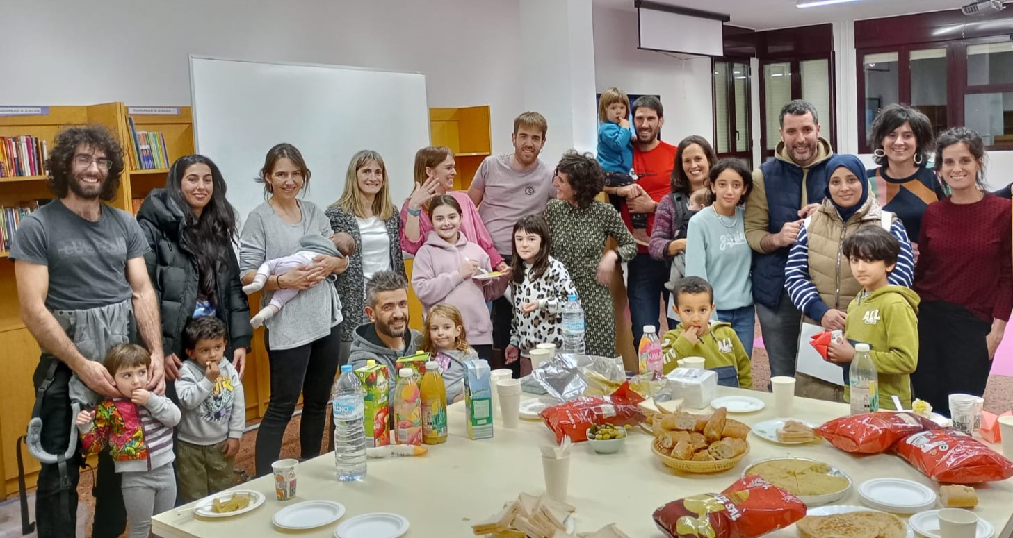 Un grupo de familias con niños posa de pie alrededor de una mesa con bebidas y refrigerios