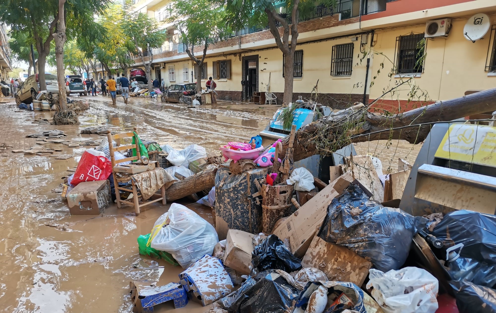 Imagen de una calle de casa bajas con el pavimento cubierto de barro y en primer plano una pila de basura y escombros también con barro