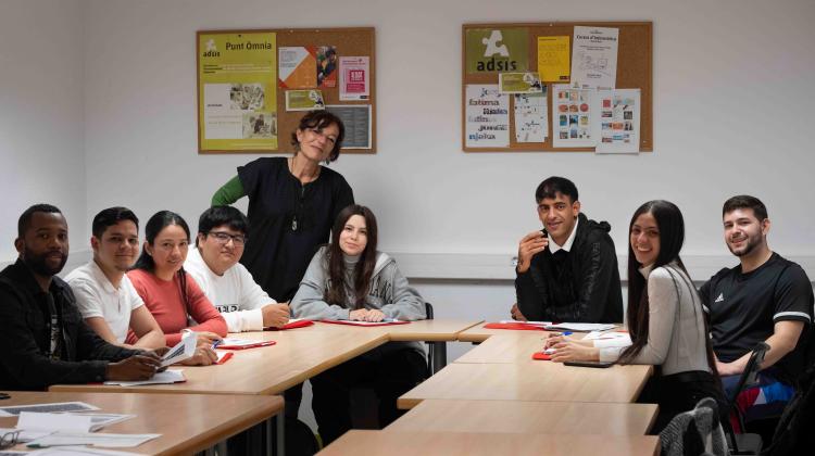 Un grupo de personas sentados en un aula mirando a cámara. Detrás, de pie, una persona formadora