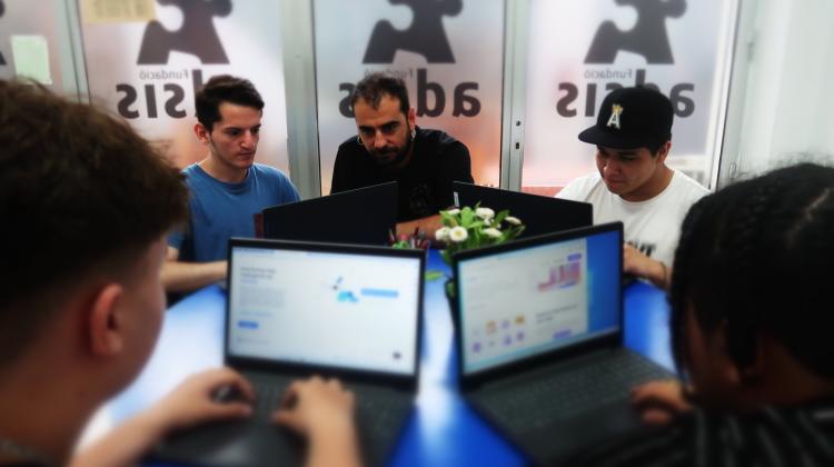 Cuatro jóvenes trabajando con sus ordenadores junto a un educador