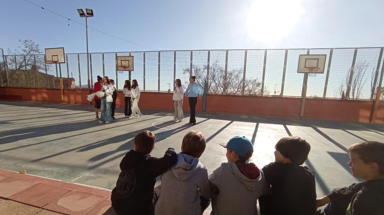 Un grupo de niños observa sentado a un grupo de adolescentes en espacio deportivo al aire libre