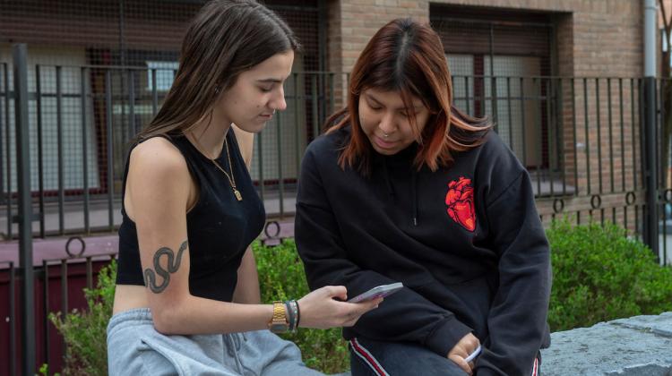 Dos jóvenes observan con curiosidad la pantalla de un móvil en un entorno urbano