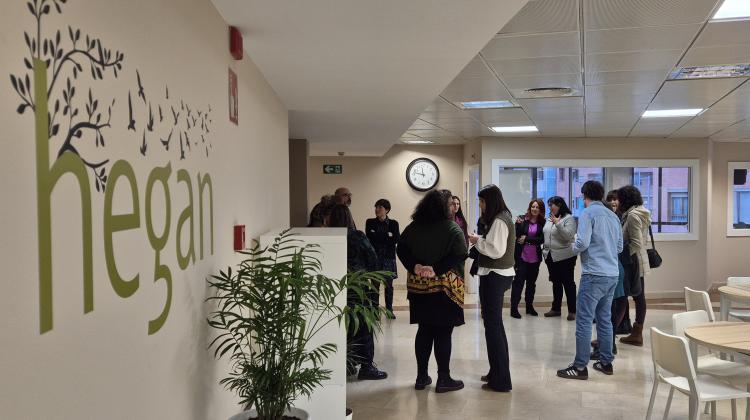 La sala principal del centro de día Hegan con el logo en la pared izquierda y un grupo de personas hablando al fodo, delante de unos despachos acristalados