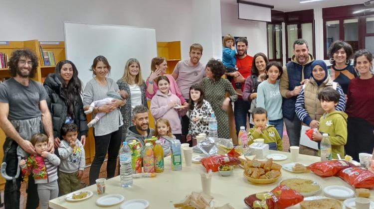 Un grupo de familias con niños posa de pie alrededor de una mesa con bebidas y refrigerios