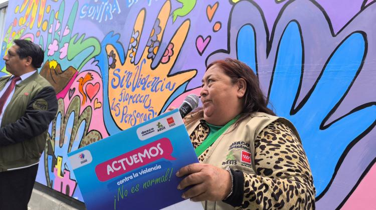 Una persona hablando con un micrófono. en la mano un cartel que lee: Actuamos contra la violencia ¡No es normal!