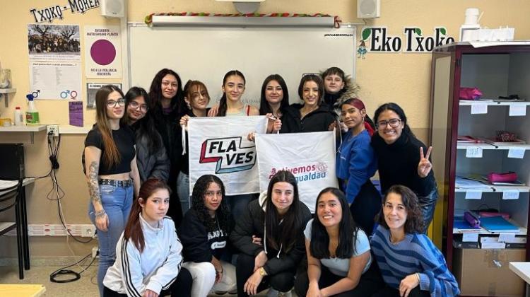 Un grupo de chicas posan en un aula mirando a cámara. Dos de ellas sujetan carteles que dicen: Flaves y Activemos por la Igualdad