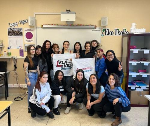Un grupo de chicas posan en un aula mirando a cámara. Dos de ellas sujetan carteles que dicen: Flaves y Activemos por la Igualdad